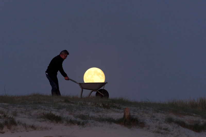 Fotografía surrealista la luna pasea en carretilla por la playa