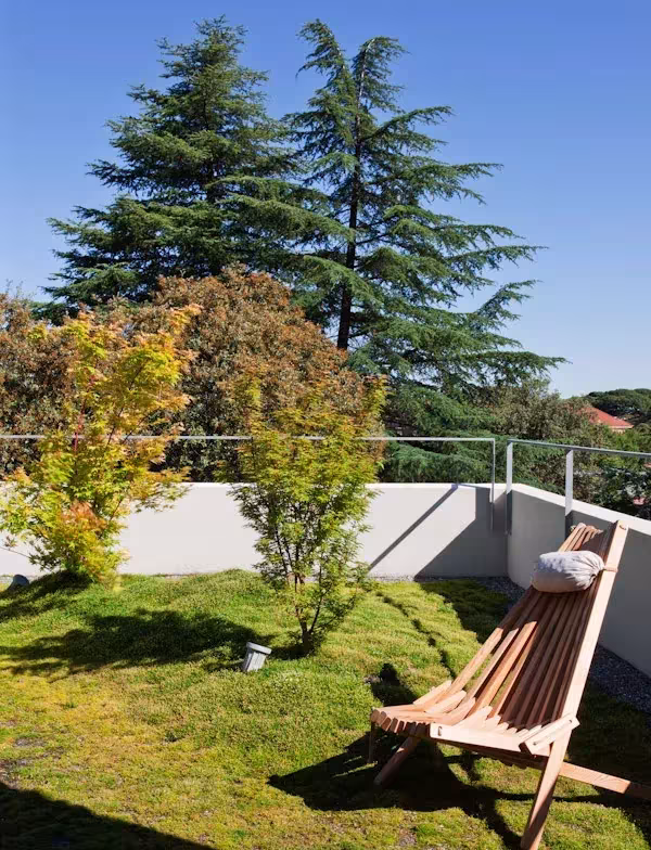 Terraza ajardinada de Ábaton con césped, tumbona de madera, arces y cedros al fondo