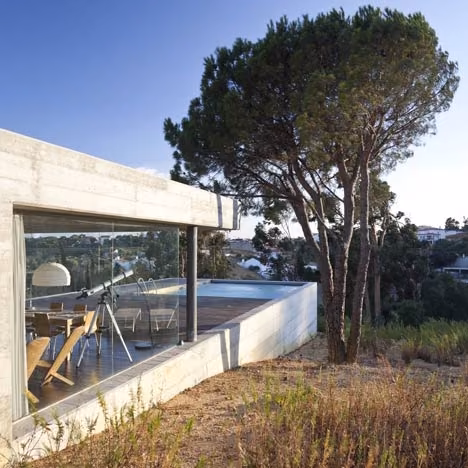 terraza Casa enterrada de Phyd Arquitectura en Pedrógão con un salón acristalado bajo un pino piñonero