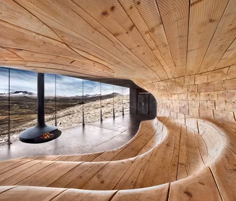 interior Interior ondulado de madera del pabellón Wild Reindeer de Snøhetta con chimenea colgante y vistas a la montaña