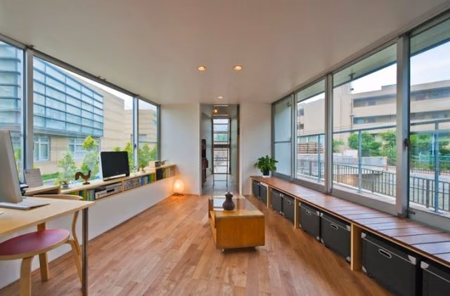vista del salón Salón alargado con suelo de madera, escritorio corrido y ventanales a ambos lados en la casa estrecha japonesa