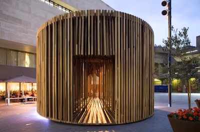 Pabellón cilíndrico Sclera de David Adjaye hecho de listones verticales de madera, iluminado en una plaza