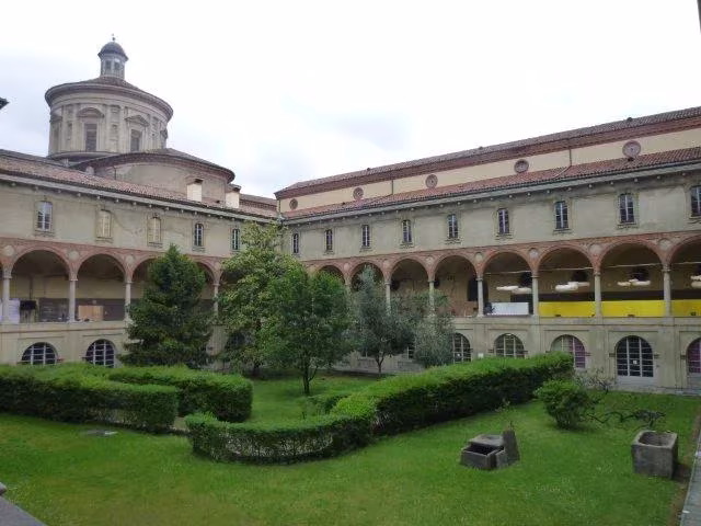 Claustro con jardín de setos y galerías porticadas, sede de una exposición del Fuorisalone en Milán