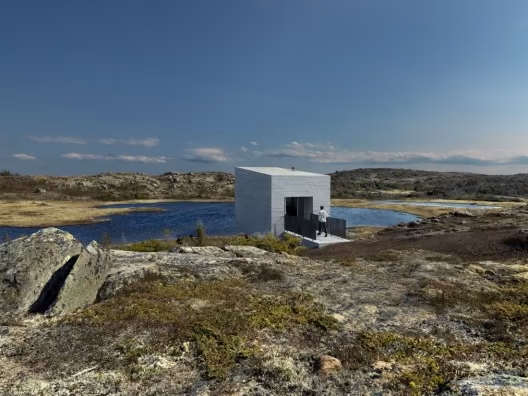 entrada Estudio blanco de Todd Saunders en la Isla de Fogo sobre rocas junto a un lago bajo un cielo azul