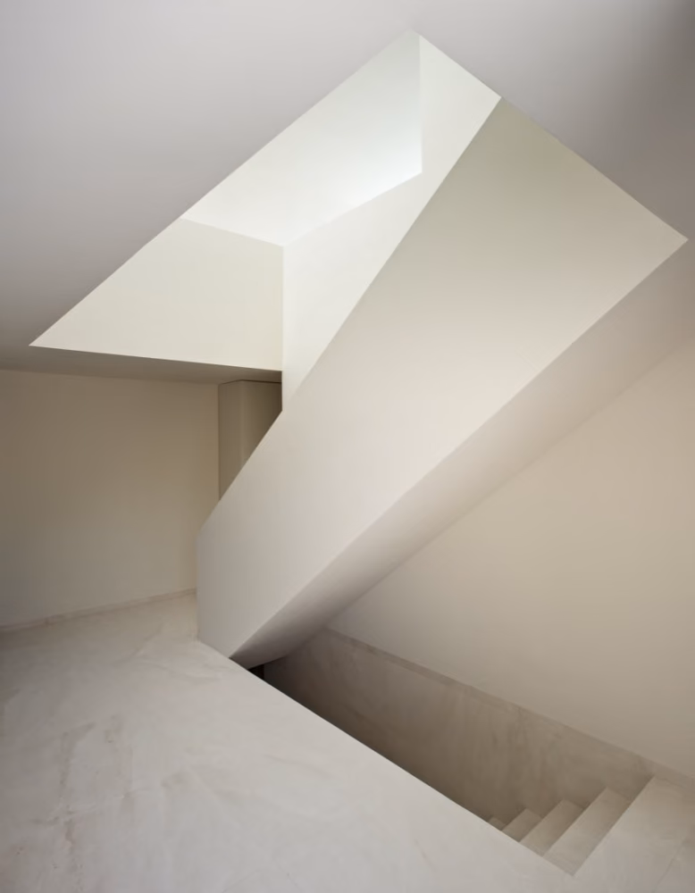 detalle del interior Escalera blanca de planos inclinados bajo una luz cenital en la casa de Fran Silvestre junto a un castillo