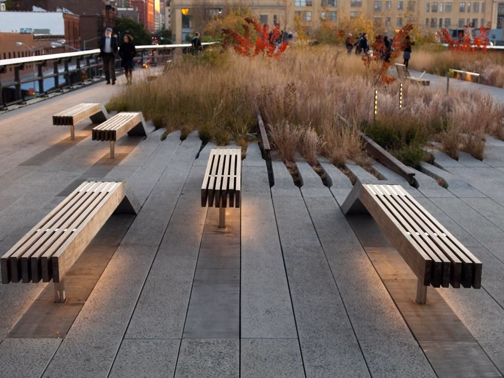 Paseo del High Line con bancos de madera que emergen del pavimento entre gramíneas y paseantes