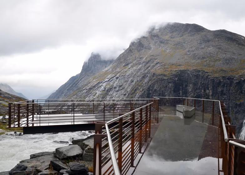 mirador Plataforma con barandillas de acero corten sobre un río de montaña bajo nubes en la ruta Trollstigen