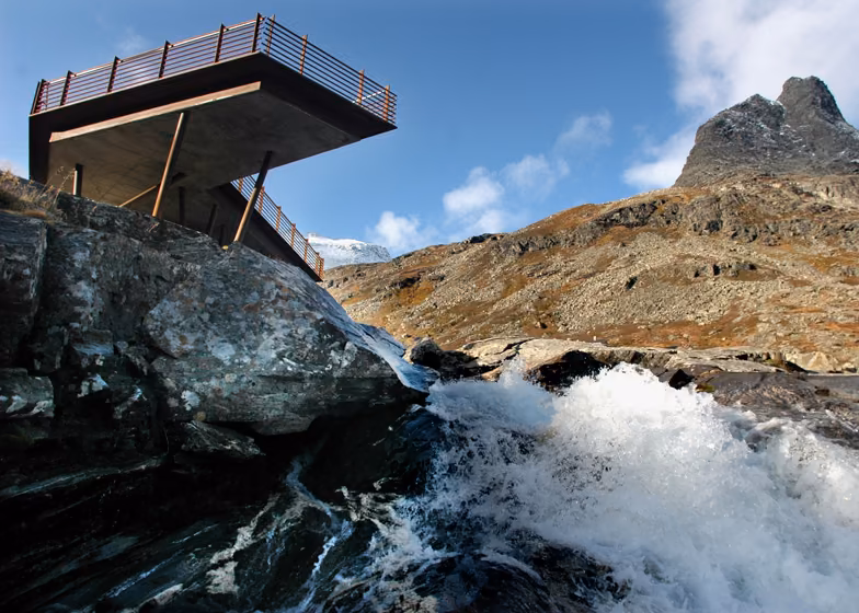 vista desde abajo Mirador volado de Reiulf Ramstad sobre una cascada que cae entre rocas en Trollstigen, Noruega