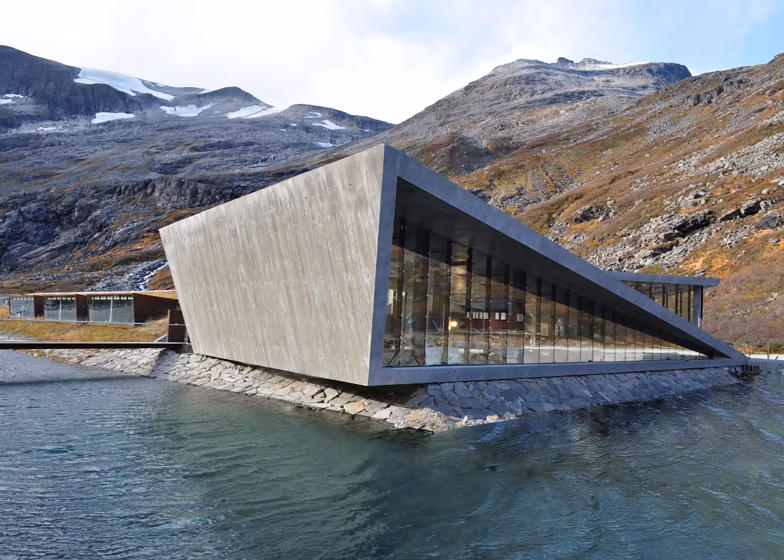 edificio principal Edificio de visitantes de Trollstigen, un volumen anguloso de hormigón y vidrio junto a un lago de montaña