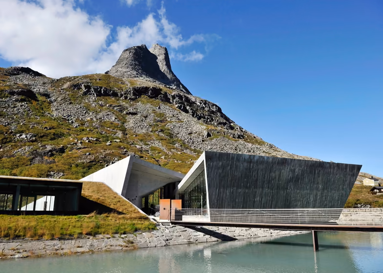 vista general del complejo Conjunto de edificios de cubierta inclinada y pasarela sobre el agua en Trollstigen bajo un pico rocoso