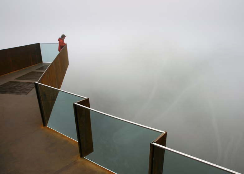 detalle del mirador Mirador de vidrio y acero corten que se asoma a la niebla con una persona en el extremo