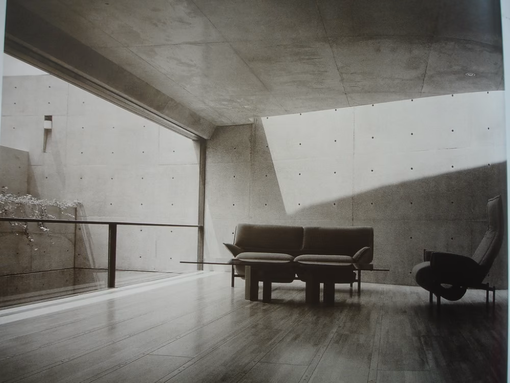 salón Salón de hormigón de la Casa Koshino con sofás oscuros y una franja de luz cenital sobre la pared