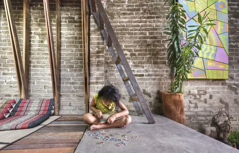 Old Market Library By TYIN Tegnestue, Min Buri, Bangkok, Thailan Niña sentada sobre un suelo de hormigón ante un muro de ladrillo y una escalera de madera, en la biblioteca de Bangkok