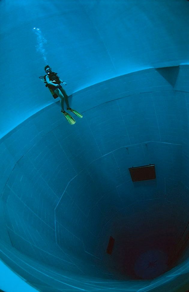Buceador descendiendo por el pozo cilíndrico de agua turquesa de la piscina NEMO 33 en Bélgica
