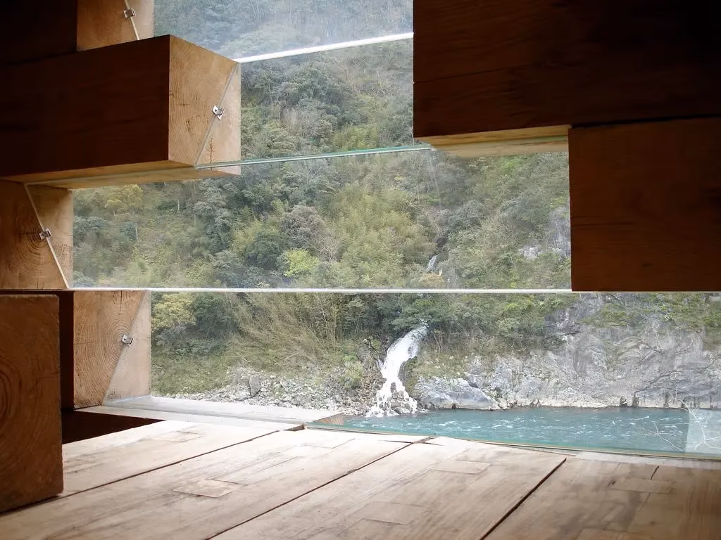 vistas Vidrio entre bloques de madera de la casa de Sou Fujimoto con vistas al río y a una ladera verde