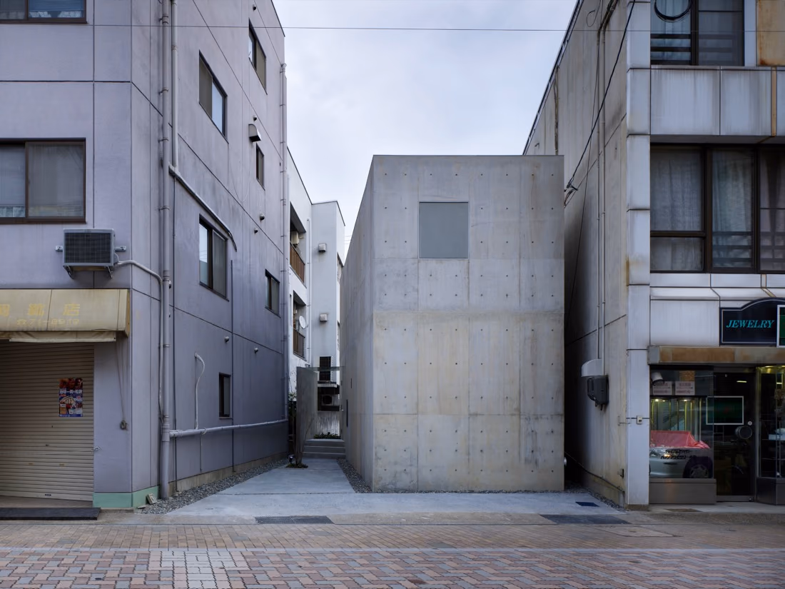 Casa Hiro, volumen cerrado de hormigón visto entre edificios de una calle japonesa