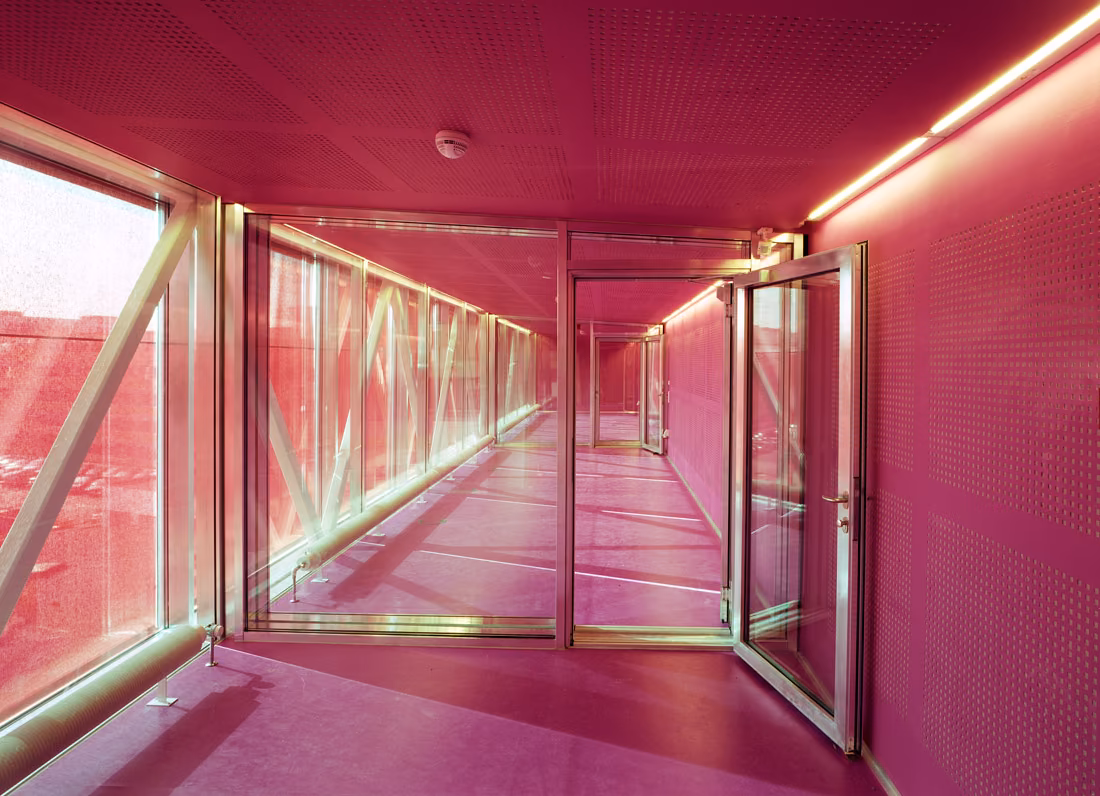 Pasarela acristalada de color magenta con estructura de celosía en el centro para jóvenes SJA