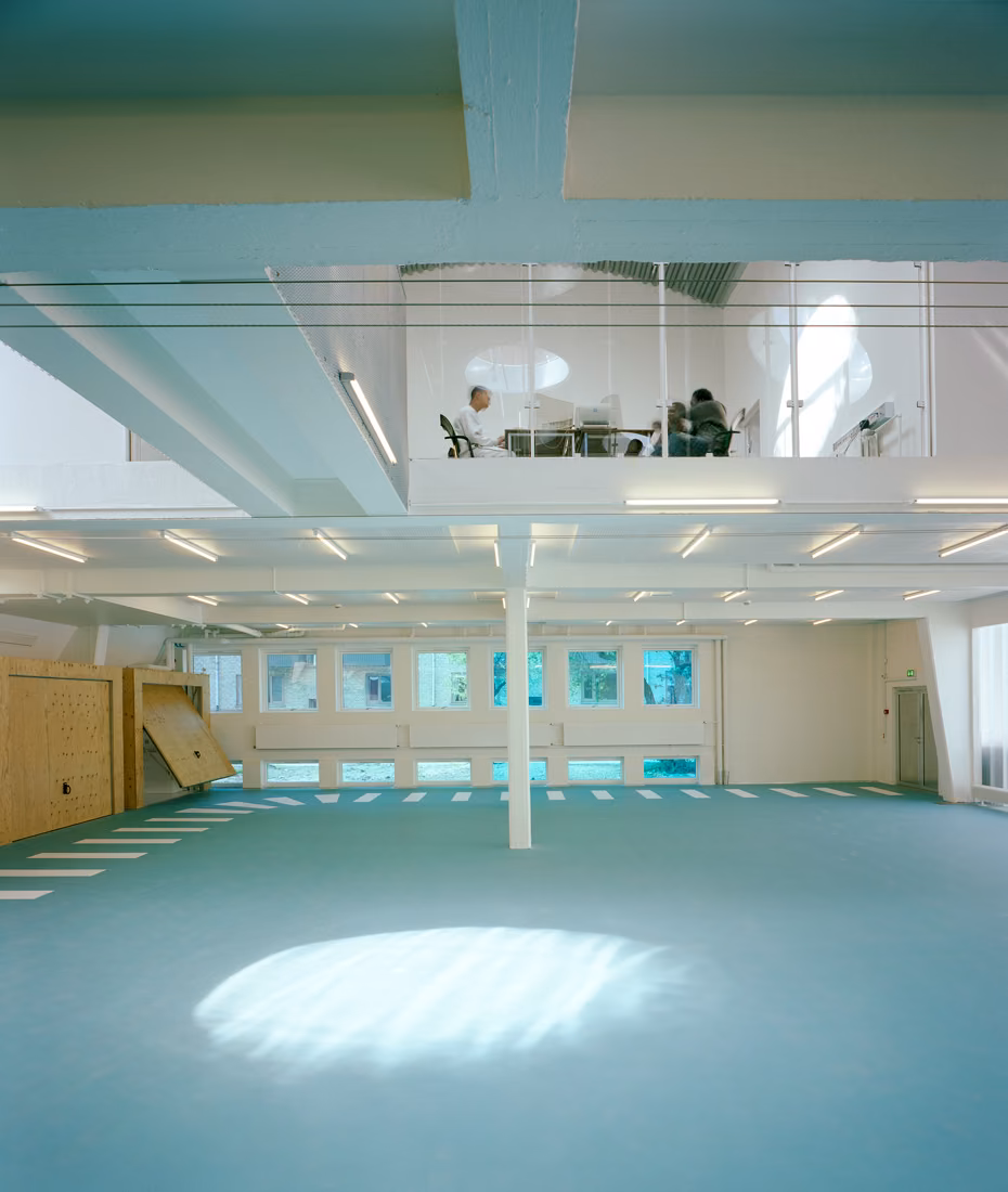 Sala diáfana del centro SJA con suelo azul verdoso, luz cenital y entreplanta acristalada