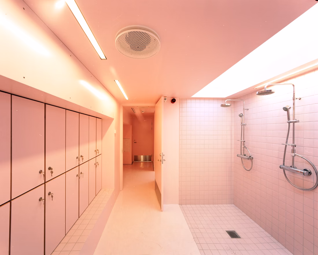 Vestuario rosado con duchas, taquillas y franja de luz cenital en el centro para jóvenes SJA