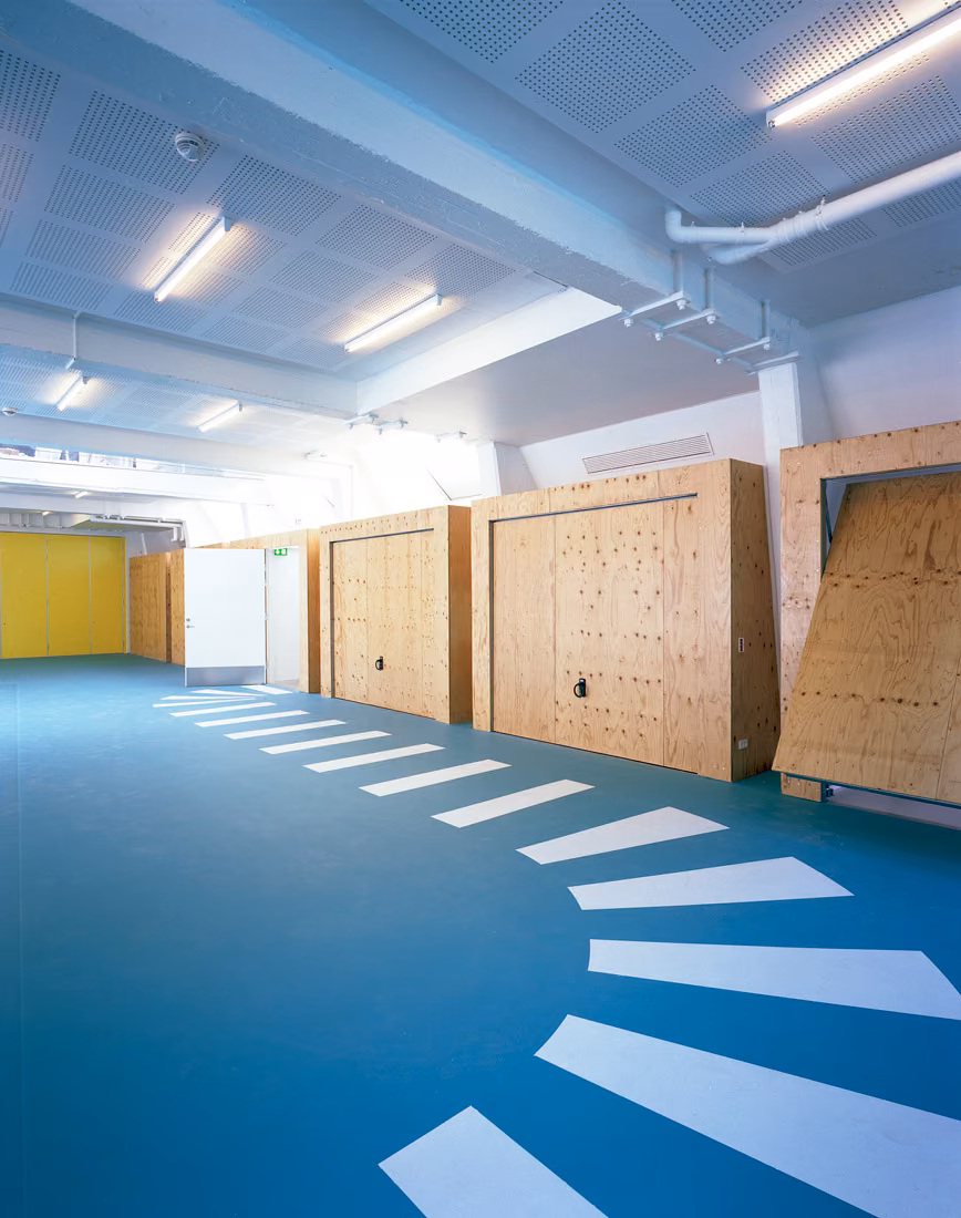 Sala del centro SJA con suelo azul de franjas blancas y módulos de contrachapado de madera