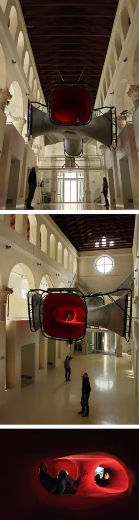 Instalación roja de Numen/For Use suspendida en un patio con arcadas y vistas de la pieza iluminada