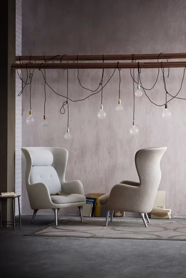 Dos butacas Ro de Jaime Hayón para Fritz Hansen en gris claro bajo una barra con bombillas colgantes