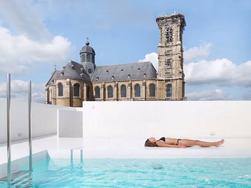 Piscina en la azotea de un antiguo colegio en Flandes, de dmvA, con una iglesia barroca al fondo