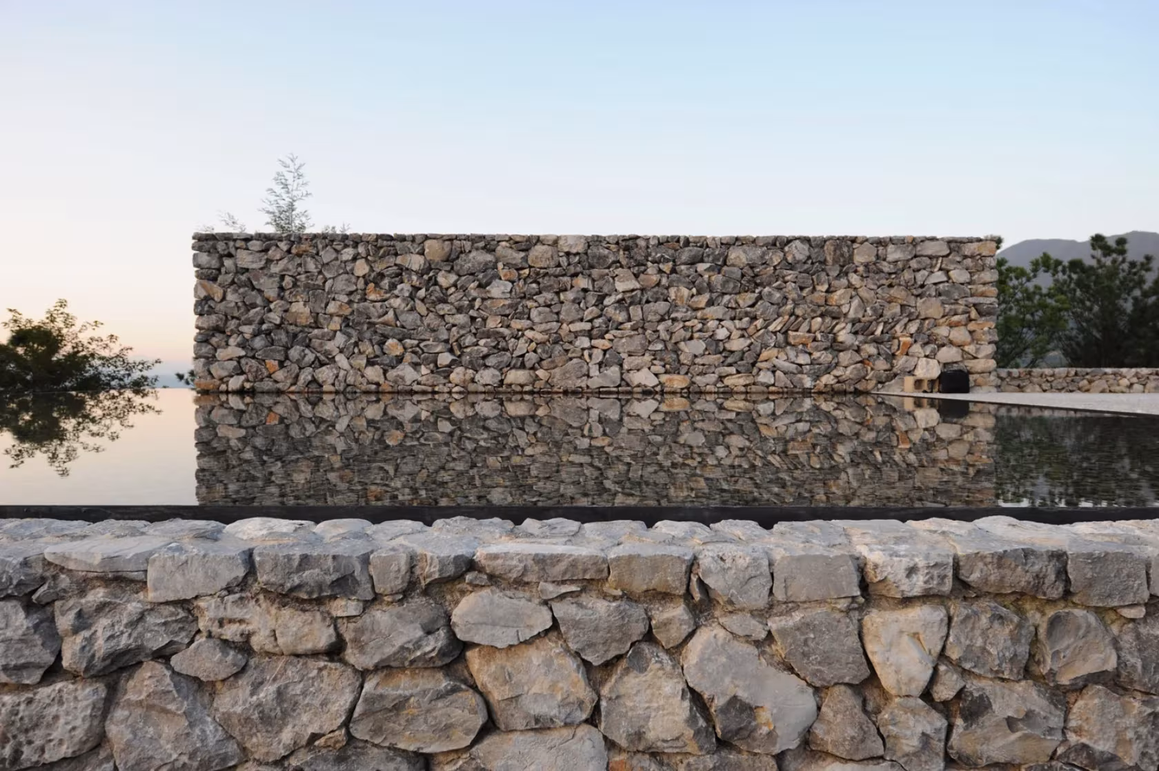 The Water House de Li Xiaodong en Lijiang: muro de piedra seca reflejado en una lámina de agua al atardecer