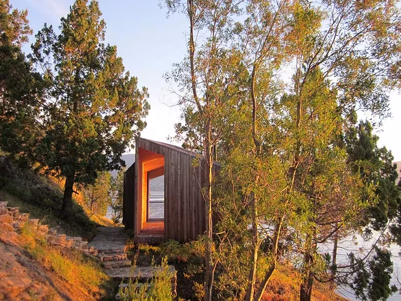 Sauna de Panorama Arquitectos junto al lago Ranco: volumen de madera oscura con ventanal iluminado entre árboles