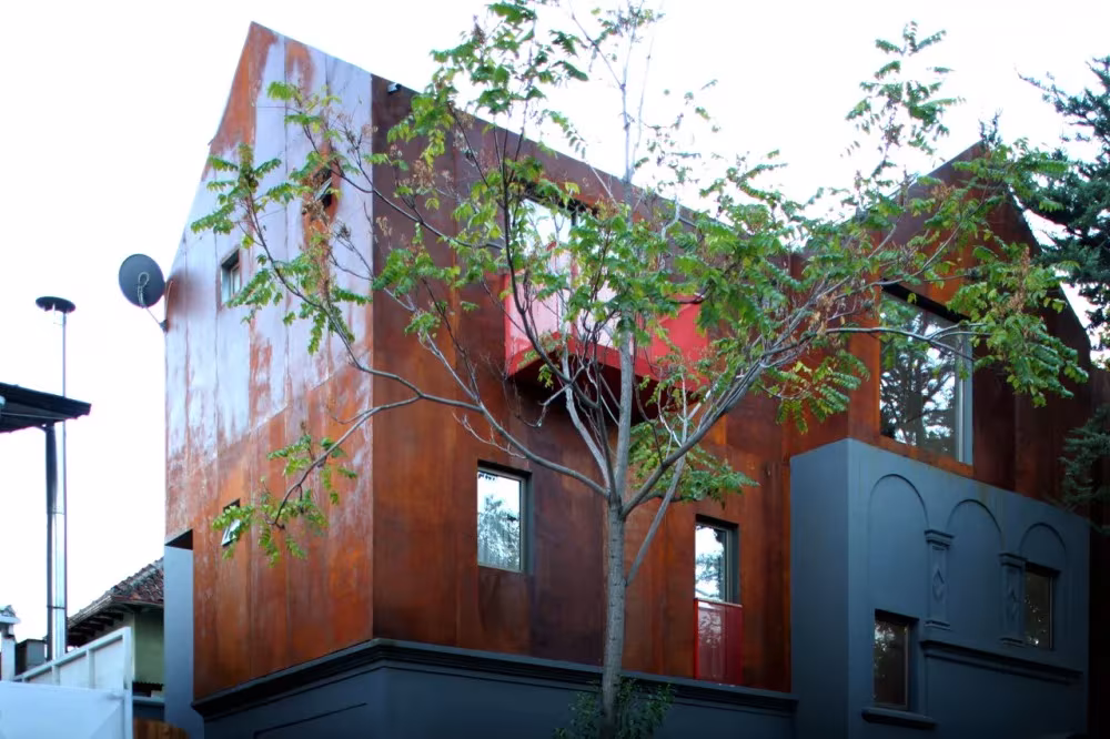 Ampliación revestida de acero corten del Hostal Caracol de FOAA Arquitectos en Santiago, entre ramas de árbol