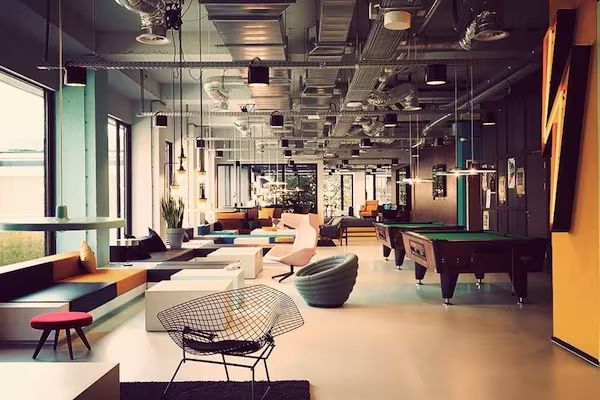 Vestíbulo de The Student Hotel Amsterdam con sofás de colores, sillas de alambre y mesas de billar