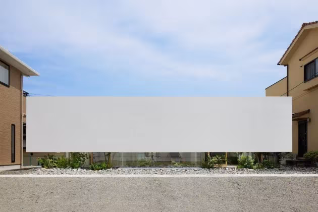Green Edge House en Japón: fachada blanca ciega que flota sobre una franja de piedras y plantas