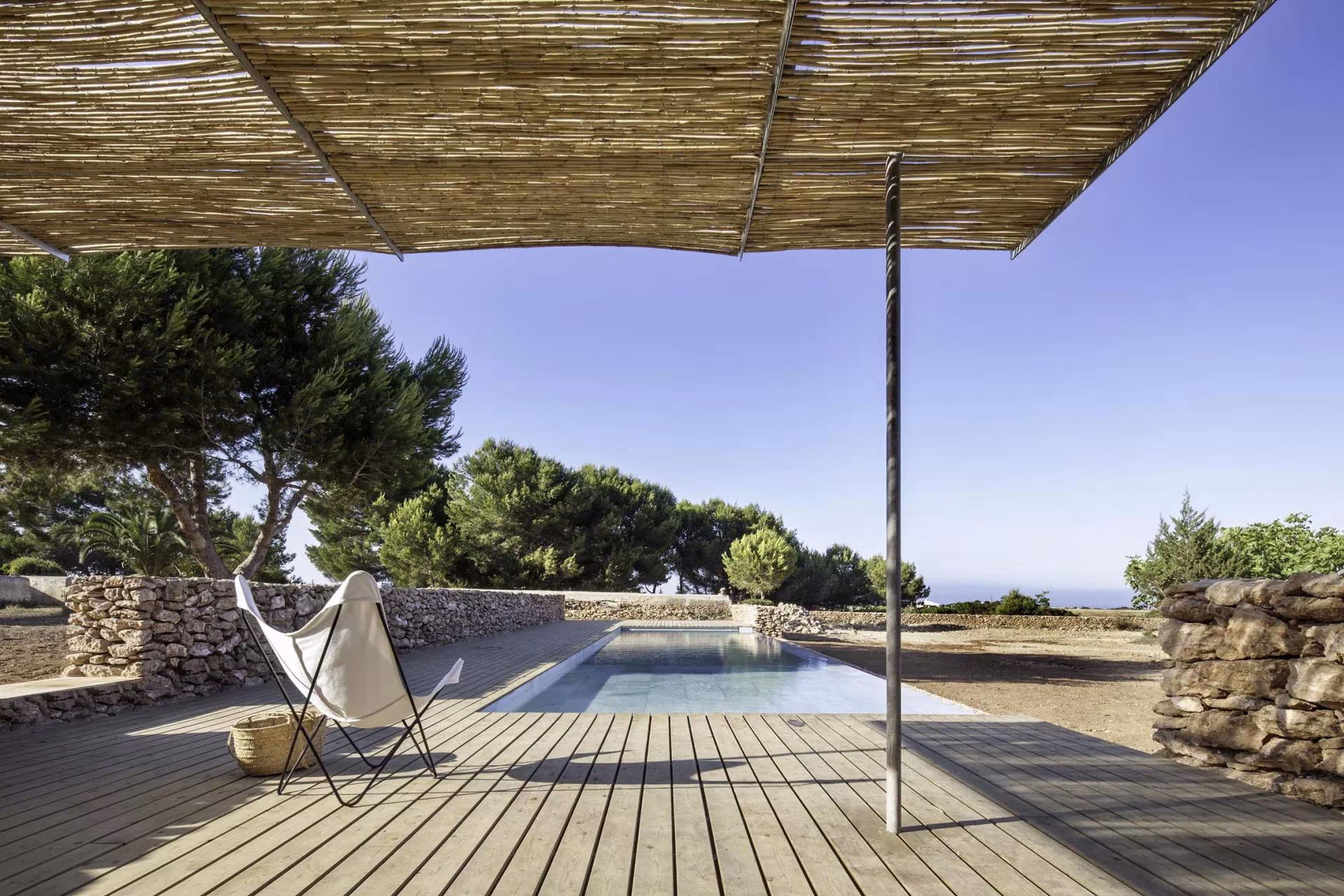 Piscina en Formentera de María Castelló: tarima de madera con sombrajo de cañizo y butaca junto al agua