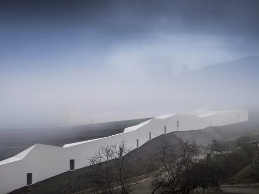 Muro blanco continuo del Centro de Alto Rendimiento de Remo emergiendo de la niebla en la ladera