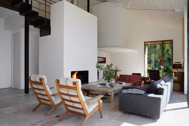 Reforma extremadura-16 Zona de estar con chimenea, butacas de madera y sofá oscuro en la reforma del establo de Gredos