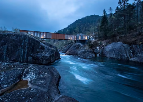 Puente Hose de Rintala Eggertsson entre rocas y aguas rápidas bajo un cielo azulado, en Noruega