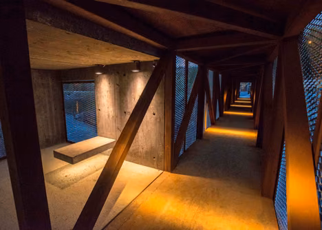 Estancia de hormigón con banco al final del Puente Hose, iluminada con luz cálida entre las cerchas de corten