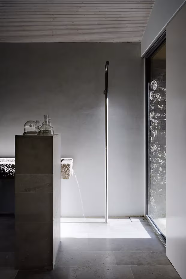 reforma extremadura-8 Baño de microcemento gris con ducha de caño de agua y ventanal en la reforma de Ábaton en Gredos