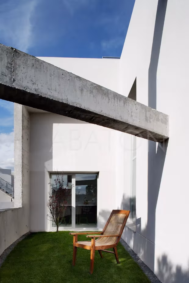 CASA 36-5 Viga de hormigón visto sobre un patio de césped con butaca de madera en la Casa 36, ático en Madrid