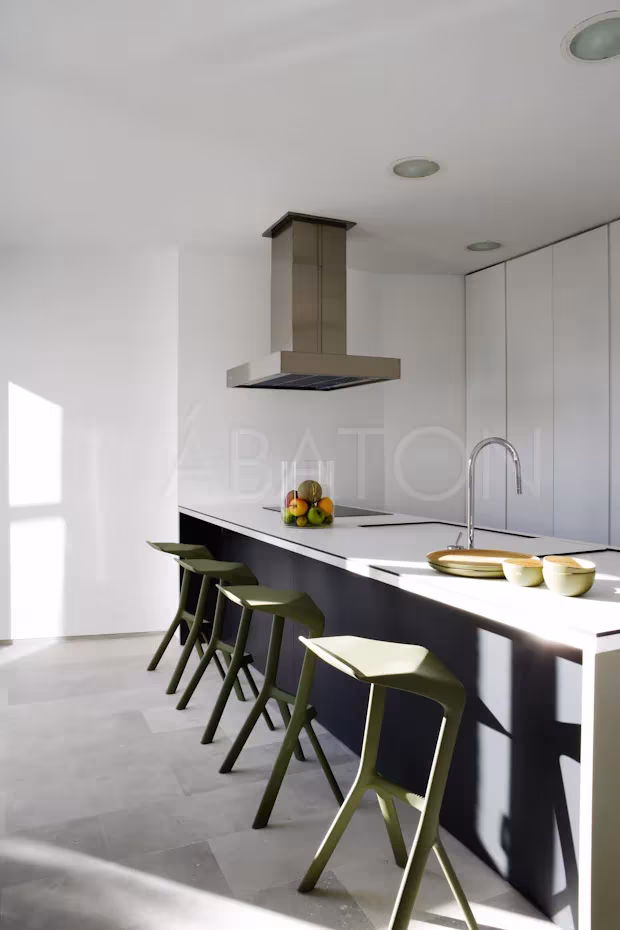 CASA 36-6 Cocina de la Casa 36 con isla oscura, taburetes verdes y campana de acero sobre suelo de piedra