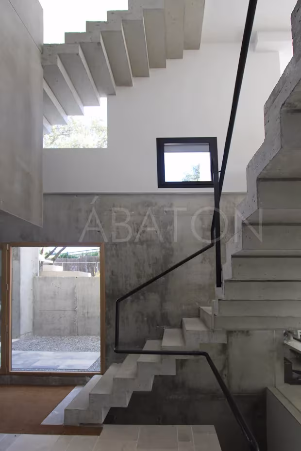Oficina-2 Caja de escalera de hormigón con peldaños volados, barandilla negra y ventana cuadrada hacia el patio inglés