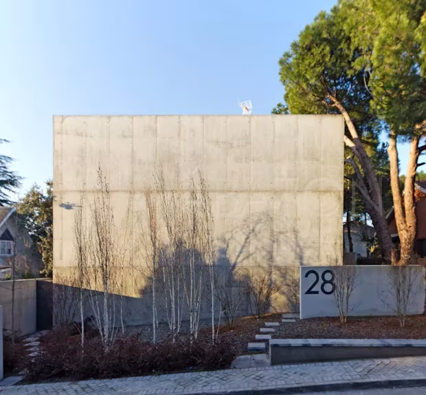 Oficina-9 Fachada ciega de hormigón visto de la oficina-vivienda-showroom de Ábaton entre pinos, con el número 28 en el muro