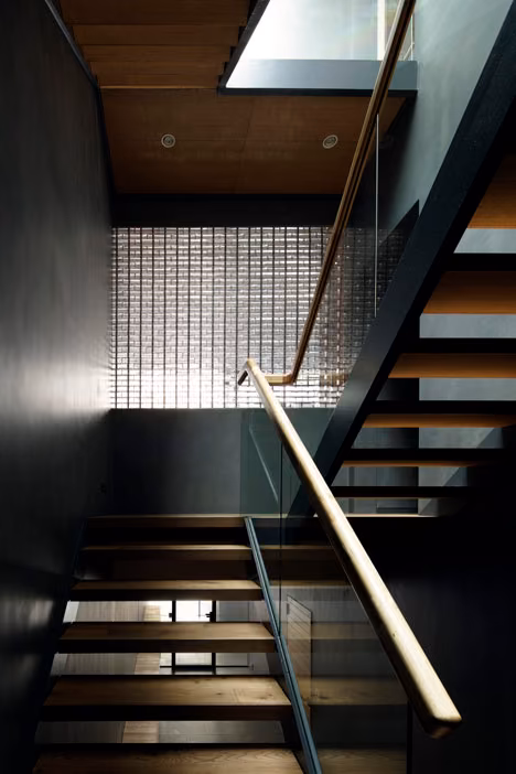 Escalera de peldaños de madera y barandilla de vidrio con el muro de bloques de cristal al fondo