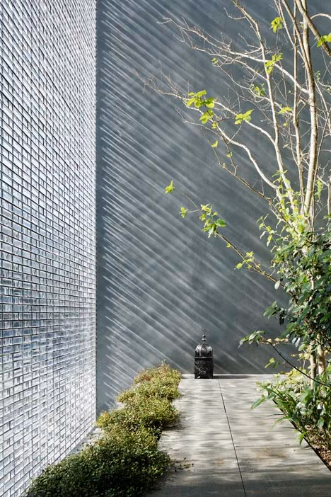 Muro de bloques de cristal translúcidos con sombras de ramas y camino de losas en la Optical Glass House