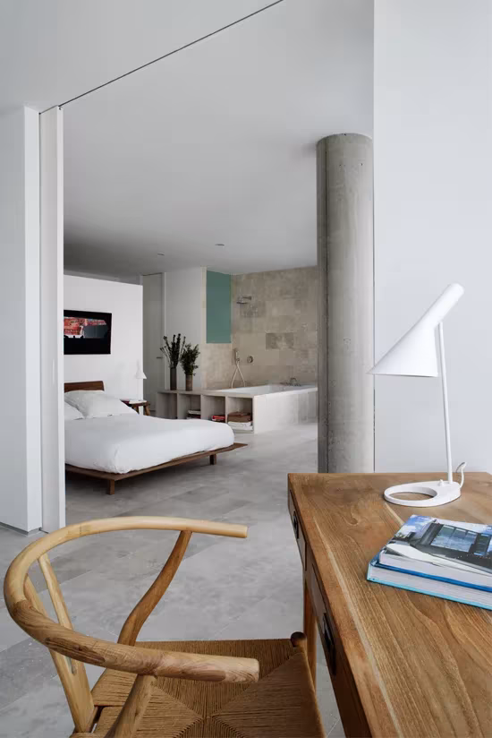 Dormitorio con cama baja y pilar de hormigón abierto al estudio, en la vivienda semicircular de Ábaton