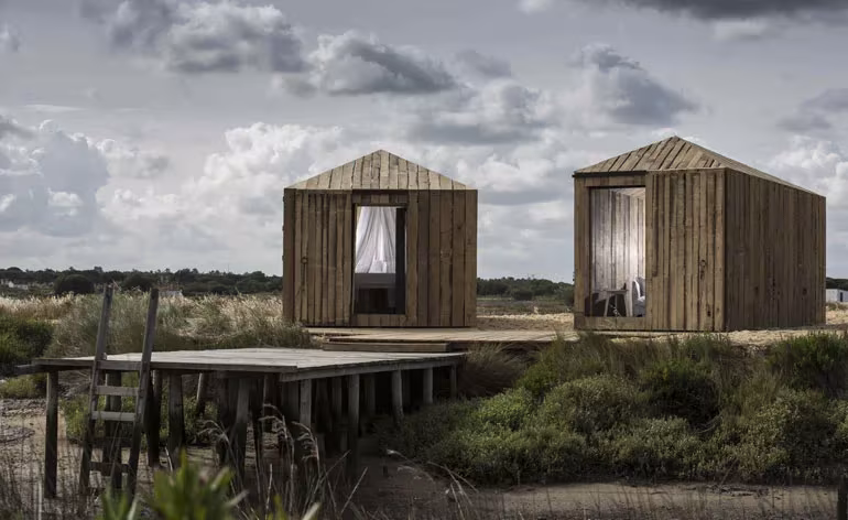 Dos cabañas de madera reciclada de Manuel Aires Mateus sobre una plataforma junto al río en Comporta