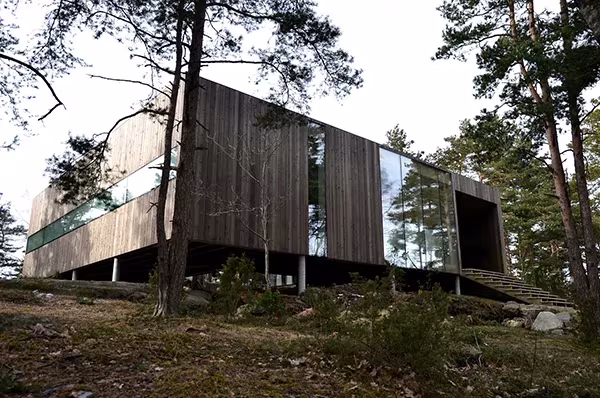 Casa Cubo de Reiulf Ramstad en Veierland, volumen de madera oscura con ventanal corrido entre pinos sobre una roca