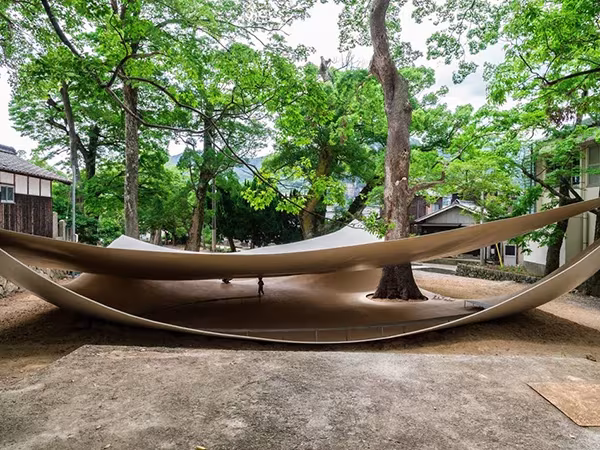 Fukita Pavilion de Ryue Nishizawa, dos láminas curvas de acero claro que rodean un árbol en un parque