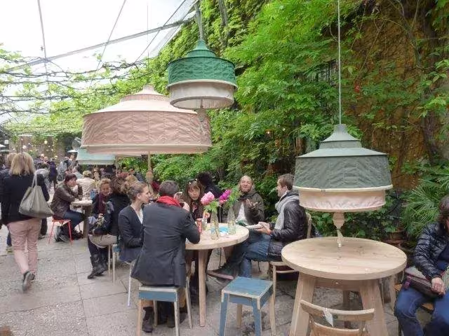 Lámparas de tela colgadas sobre mesas bajo una pérgola vegetal en el Salone del Mobile de Milán