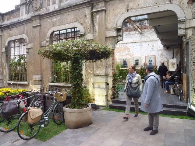 Patio de una antigua nave industrial con árbol en maceta y bicicletas durante la Feria del Mueble de Milán